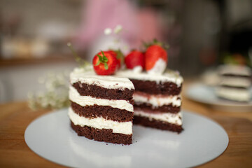 A pastry chef holds a chocolate cream cake on a stand, decorated with strawberries.
