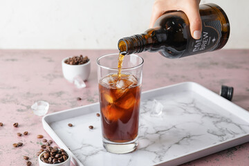 Pouring of cold brew coffee from bottle into glass on table