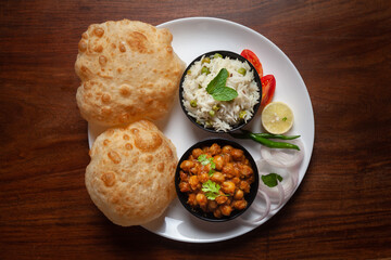 Chickpeas masala (Spicy chola or chhole curry) and Bhatura or Puri garnished with fresh green coriander and ingredients. A Classic Indian typical Panjabi street food.
