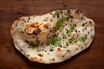 Close-up of fresh, hot tandoori roti or naan garnished with black till and green fresh coriander leaves. A typical, traditional north indian panjabi food.