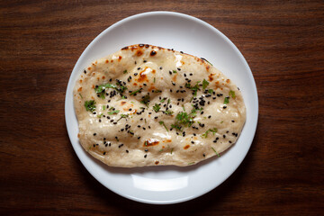 Close-up of fresh, hot tandoori roti or butter naan garnished with black till and green fresh coriander leaves. A typical, traditional north indian panjabi food.