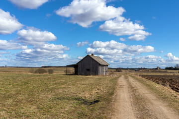 An old abandoned small wooden house in the field blue sky white clouds, barn or scary concept.