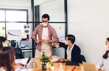 Asian business man in quarantine for coronavirus wearing protective mask shaking with elbows in new normal with group of professional business meeting and discussing strategyat at office
