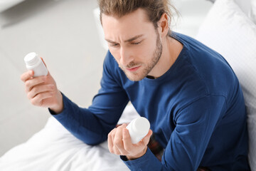 Handsome young man with pills in bedroom