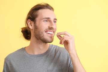 Handsome young man taking pills on color background