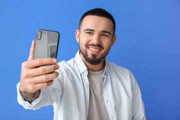 Handsome young man taking selfie on color background