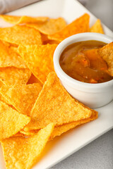 Plate with tasty nachos and sauce on light background