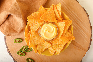 Plate with tasty nachos and sauce on light background