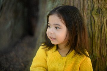 A cute young girl looking away by a tree