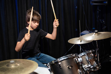 The boy learns to play the drums in the studio on a black background. Music school student