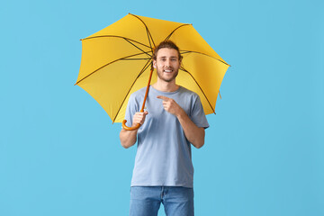 Handsome young man with umbrella on color background