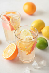 Glasses of tasty cold lemonade and citrus fruits on light background