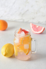 Mason jar of tasty cold lemonade and citrus fruits on light background
