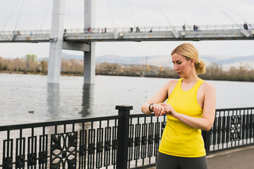 Beautiful young woman turns on sports modern smart watch before sports training fitness jogging on the city street