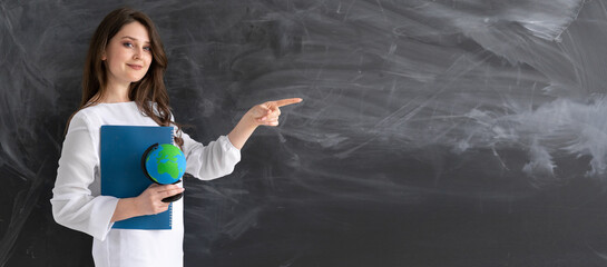 Young teacher or student millennial girl standing with a globe and a notebook in front of a black...