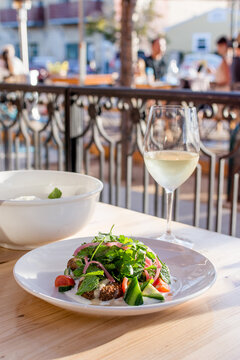 Fresh salad on a table with a glass of white wine at an outdoor cafe, with a wrought iron fence in the background. Bright cheerful image