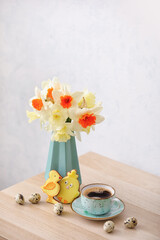 Obraz na płótnie Canvas Vase with beautiful daffodils, quail eggs and cup of coffee on table against light background