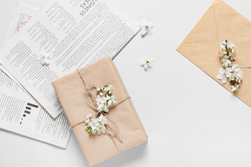 Beautiful blooming branches, gift box and newspaper on light background