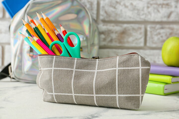 Pencil case and stationery on light table near brick wall