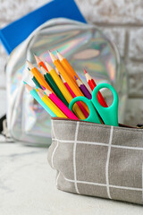 Pencil case and stationery on light table near brick wall