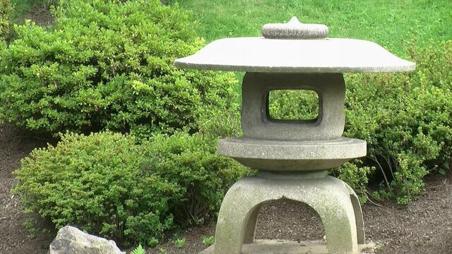 A Japanese snow lantern (yukimi doro) stands amid azalea bushes in a Japanese garden.