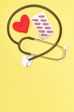 Vertical. Stethoscope with a red heart and pills on a yellow background