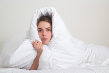 Funny woman wrapped in soft blanket sitting on bed. Smiling girl sitting in bed and smiling at home.