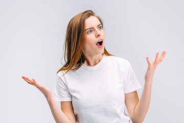 shocked woman with open mouth indignantly waves her hands on gray background.