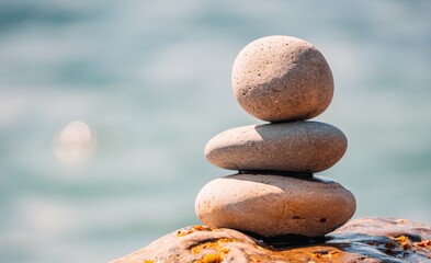 Balanced pebble pyramid on the beach on a sunny day. Abstract Sea bokeh on the background. Selective focus. Zen stones on the sea beach, meditation, spa, harmony, calmness, balance concept