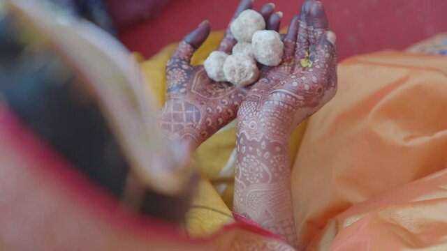 Bride holding ladoo sweets on her hand with mehndi. Woman with tasty white ladoos. 