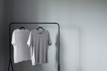 two t-shirts of neutral colors on  black hanger against  gray wall