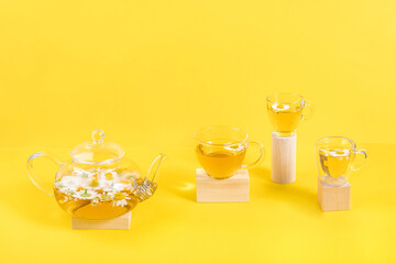 Three cups of camomile tea, transparent teapot on wood geometric shape, yellow background. Creative concept Natural Chamomile Tea. Top view Flat lay