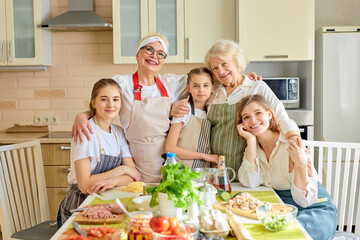 Portrait Of Sweet Pretty Different Generation Family, Females At Day time in kitchen At Home. Good-lookign Senior Ladies Hugging Children, Teaching To Cook, Having Fun Together, Copy Space