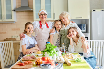 Portrait of smiling women children guhhing each other in bright cozy kitchen, posing at camera, spending ggod holidays together, wearing aprons. copy space