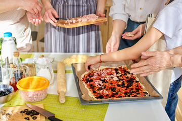 Cropped female hands adding ingredients, prepading tasty pizza for whole family. close-up photo of women at home, preparing meal, helping. concept pastimes of isolation time in quarantine mode
