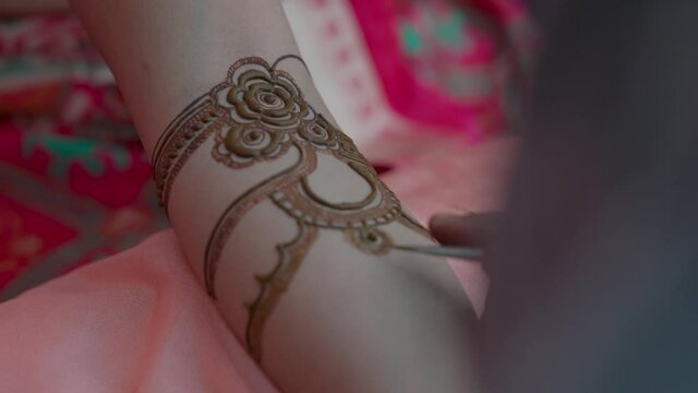 Woman gets her hand tattooed with traditional mehndi at Indian wedding ceremony.