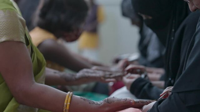  Women get their hands tattooed with traditional henna mehndi at Indian wedding.