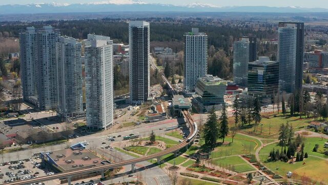 Aerial Zoom In on a Skytrain in Motion at King George Station, Surrey BC Canada. Fast Drone View from Overhead of Subway Light Rail Train Pulling into a Modern Passenger Transit Hub on a Sunny Day