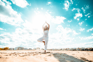 Senior woman doing yoga exercise tree pose on beach at sunset - Calm and meditation concept