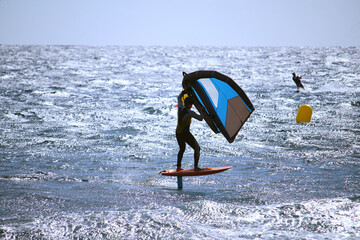 Windsurfer wing foiling at the ocean glistening in the sun, in backlight (Tenerife, Spain)