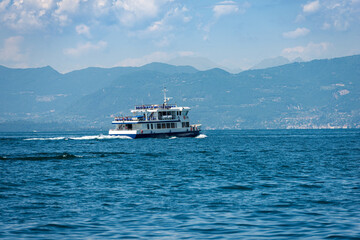 Ferry boat in motion in front of the small village of Bardolino on Lake Garda (Lago di Garda), Verona province, Veneto, Italy, Europe. On the horizon the coast of Lombardy with the mountains.
 - obrazy, fototapety, plakaty
