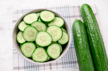 Pile of fresh sliced cucumbers in bowl on white background