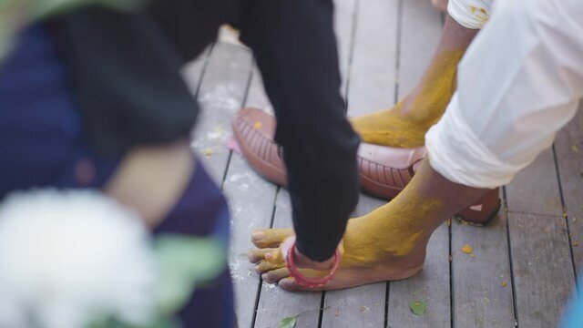 Slow motion shot of Haldi ceremony at North Indian traditional wedding. Turmeric paste being smeared on groom&rsquo;s legs at Indian marriage function.
