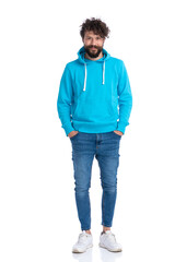 curly unshaved man with blue sweatshirt holding hands in pockets