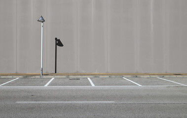 Gray concrete wall with a streetlight and its shadow. Sidewalk and asphalt road with parking in...