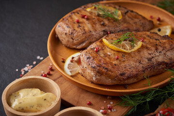 Grilled chicken breast on a wooden board and vegetables with tomatoes and mushrooms, potato, garlic, herbs, lemon, rosemary, salt  on a stone background with space for text