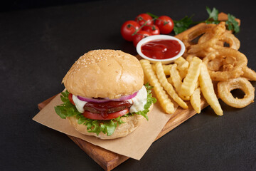 Homemade hamburger or burger with fresh vegetables and cheese lettuce and mayonnaise served, French fries on pieces of brown paper on black stone table . concept of fast food and junk food