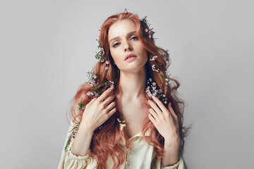 Portrait of a young woman with long red curly hair. Pink flowers in hair. Natural cosmetics and...