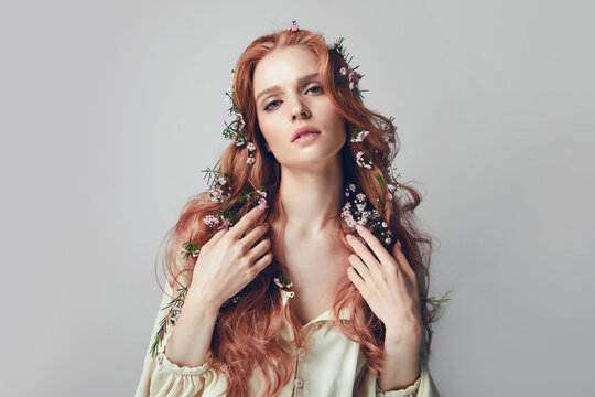 Portrait of a young woman with long red curly hair. Pink flowers in hair. Natural cosmetics and make-up. Hair care.
