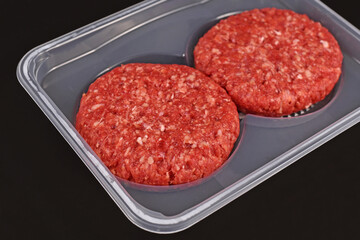 Round raw burger patties in package on dark background